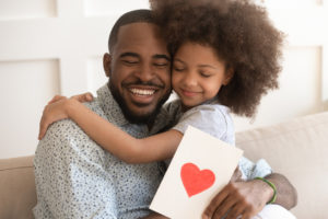 A father and daughter embrace as he holds a greeting card from her.