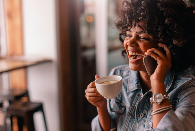 A woman laughs as she talks on the phone while holding a mug