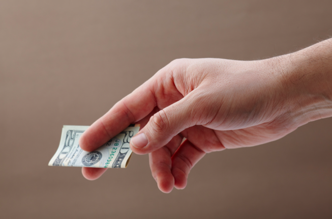 An outstretched hand is shown holding a folded $20 bill